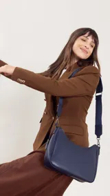 Bandolera de cuero sintético color marrón, con cierre trasero y división interna. Incluye correa de galón ajustable y un pequeño charm colgante.