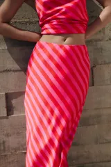 Falda midi fluida confeccionada en tejido satinado con estampado de rayas diagonales en tonos rojo y rosado, y cintura elástica.