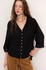 Camisa negra de manga larga con escote en V, cierre frontal de botones claros y detalles de encaje en las mangas y puños.
