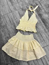 Conjunto de top halter y minifalda con volados, ambos de tela broderie color amarillo pastel.