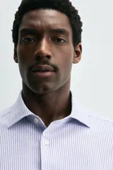 Camisa de manga larga, color celeste con finas rayas verticales blancas, cuello italiano y cierre frontal de botones.