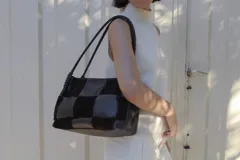 Cartera de hombro con diseño de patchwork que alterna paneles de cuero liso y gamuza en color marrón oscuro. Presenta doble asa trenzada y estructura rectangular.