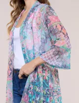 Cardigan largo de tul semitransparente color verde, con estampado patchwork y bordados florales en relieve. Presenta diseño de frente abierto con solapas fluidas y mangas tres cuartos acampanadas.