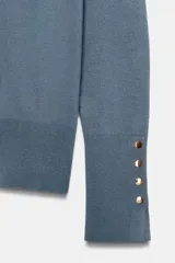 Jersey de punto liso color negro, con cuello redondo y manga larga. Presenta una hilera de cuatro botones dorados decorativos en el puño de cada manga.