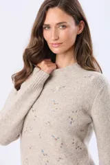 Buzo tejido de punto en color beige, con cuello redondo, mangas largas y puños acanalados. Presenta un delicado diseño bordado con motivos florales dispersos en el frente y una etiqueta de cuero sintético en el ruedo.