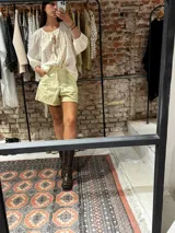 Short de lino en color celeste, con diseño de tiro alto, cierre frontal con botón a la vista y costuras decorativas verticales en el frente.