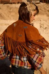 Chall de gamuza natural con diseño de flecos largos en todo el borde y detalle de pins metálicos decorativos en la parte frontal.