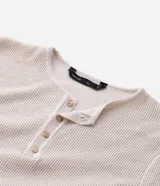 Remera de manga larga estilo Henley, confeccionada en tejido texturizado color beige, con cuello redondo y cierre frontal parcial de botones.