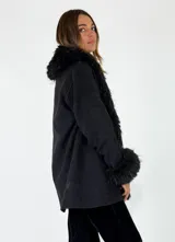 Chaqueta midi color crudo con detalles de piel sintética en el cuello y los puños. Presenta un diseño abierto con bolsillos laterales y una textura suave.