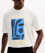 Remera de corte boxy confeccionada en algodón, con cuello redondo y manga corta. Presenta una estampa frontal con diseño artístico abstracto en tonos azules y marrones sobre un fondo claro.