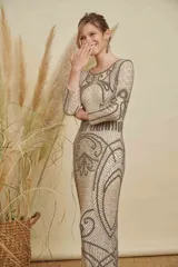 Vestido largo de fiesta color beige, con mangas largas y cuello redondo. Presenta un intrincado diseño bordado con canutillos y lentejuelas en tonos plata y gris, creando patrones geométricos y ornamentales en toda la prenda.