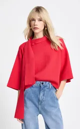 Blusa de punto color rojo con diseño de cuello asimétrico que incorpora una bufanda integrada. Presenta mangas anchas de largo tres cuartos y un corte holgado.