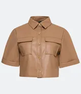 Camisa de manga corta confeccionada en cuero sintético color tostado, con cuello camisero, cierre frontal con botones en forma de corazón y dos bolsillos con solapa en el pecho.
