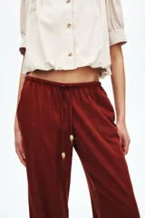 Pantalón de pierna recta en tejido liviano mezcla de lino y viscosa, color rojo. Cuenta con cintura elástica de tiro bajo, cordón de ajuste con cuentas decorativas en los extremos y bolsillos laterales al bies.