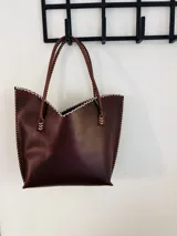 Cartera tipo tote de cuero color chocolate, con manijas largas, borde superior en corte en V y costuras artesanales contrastantes en color blanco en todo el contorno.