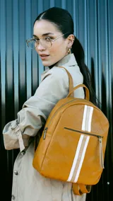 Mochila de cuero sintético color mostaza con diseño capitoneado. Presenta una franja vertical central en tonos blanco y beige, bolsillo frontal con cierre y correas regulables.