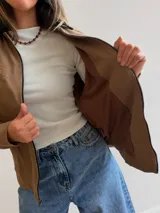 Campera de gabardina color beige con cierre frontal y cuello en contraste color negro. Presenta un diseño minimalista con bolsillos delanteros funcionales y calce cómodo.