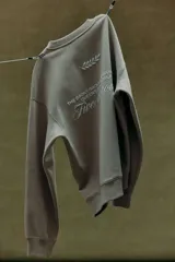 Buzo color beige de corte holgado, con cuello redondo y puños y ruedo acanalados. Estampado pequeño con la frase "New York" y un diseño de hojas en el pecho.