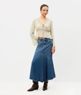 Pollera midi de jean azul, de tiro medio con pretina y pasacintos. Presenta un recorte diagonal en la parte inferior decorado con pequeñas tachas metálicas.