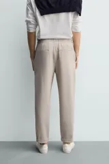 Pantalón jogger color beige de tejido transpirable y elástico con cintura elástica ajustable con cordón, bolsillos frontales y bajo con vuelta.