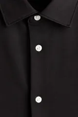 Camisa negra de punto elástico con cuello italiano, cierre frontal de botones y mangas largas.