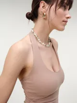 Top halter cropped de tejido rib color beige, con escote redondo pronunciado y espalda descubierta, de calce entallado.