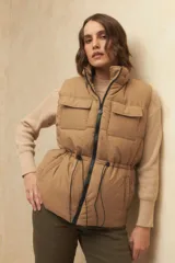 Chaleco puffer color crema, con cuello alto, cierre frontal y cuatro bolsillos con solapa. Cuenta con cintura ajustable con cordón.