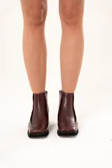 Bota corta de cuero color bordó, con punta cuadrada, taco bloque y plataforma. Presenta cierre lateral interno y detalle de ribete en la capellada.