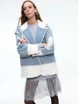 Chaqueta de denim con diseño patchwork, que combina paneles de jean azul claro con secciones de tela blanca acolchada. Presenta solapas amplias, bordes deshilachados, cierre frontal con botones y parches decorativos en las mangas.