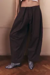 Pantalón de gabardina impermeable color marrón chocolate, con silueta amplia y relajada. Presenta cintura elastizada con pinzas delanteras que aportan volumen y movimiento a la prenda.