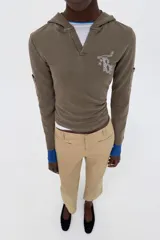 Sudadera de algodón color gris oscuro con capucha, manga larga y detalle de texto con aplicación de brillos en el pecho. Presenta un diseño con bolsillos laterales en las mangas y bajo recto.