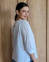 Remera blanca con cuello en V, cuerpo de algodón y mangas abullonadas de encaje bordado con puños elásticos.