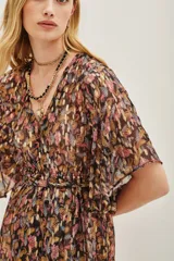 Vestido largo con estampado de hojas en tonos otoñales y metalizados, escote en V con botones frontales y mangas mariposa amplias. Presenta un lazo ajustable a la cintura y abertura frontal en la falda.