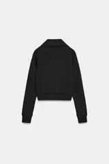 Chaqueta de felpa negra con cuello solapa, manga larga con puño, bolsillos de plastrón en el delantero y cierre frontal con cremallera.