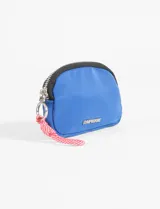 Monedero azul de poliéster con cierre superior, herrajes metálicos plateados, detalle de marca metálica en el frente y cordón decorativo rojo y blanco en la argolla lateral.