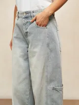Jean de corte wide leg en color celeste claro con lavado desgastado. Presenta un diseño de cinco bolsillos, incluyendo bolsillos laterales tipo cargo, cierre frontal con botón y bragueta, y costuras reforzadas en las piernas.