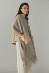 Chal de lana fina sin teñir con diseño de cuadros sutiles, cierre frontal con alamar y bolsillos de cuero metalizado. Presenta terminaciones con flecos en el ruedo y un calce estructurado en los hombros.