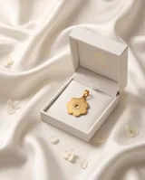 Dije con forma de flor de seis pétalos, con centro circular calado y detalle grabado, acabado en tono dorado.