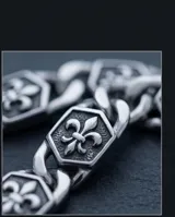Pulsera de eslabones de acero inoxidable con placas hexagonales decoradas con el símbolo de la flor de lis en relieve y acabado envejecido. Cuenta con un cierre de mosquetón robusto.