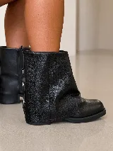 Bota corta de cuero gamuzado color marrón, con diseño de polaina superpuesta y detalle de hebillas metálicas en la parte posterior del talón. Cuenta con suela plana de goma negra y horma amplia.