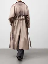 Gabardina cruzada color beige con efecto envejecido, de corte recto y largo midi. Presenta doble solapa en el lado derecho, doble botonadura frontal, bolsillos laterales, mangas largas con trabillas en los puños y canesú amplio en la espalda.