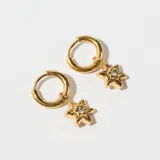 Par de caravanas doradas con forma de aro y dije colgante con forma de estrella de ocho puntas con un cristal en el centro.
