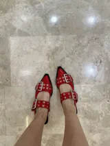 Stilettos rojos charol con punta fina, dos tiras con hebillas y detalles de tachas plateadas. Destalonados.