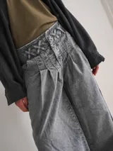Pantalón wide leg de tiro medio confeccionado en denim blanco. Presenta una cintura con diseño de pasacintas entrelazadas, cierre frontal y bolsillos laterales. Su diseño de pierna amplia ofrece una caída fluida con volumen.