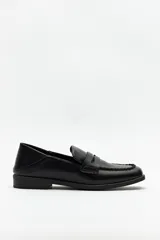 Mocasín de cuero sintético negro con punta cuadrada, detalle de costuras visibles en la capellada y taco bajo.