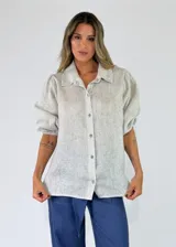 Camisa beige de lino con cuello camisero, cierre frontal de botones y mangas cortas abullonadas con puños elásticos.