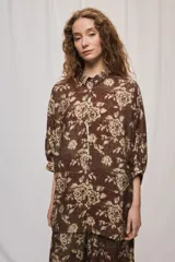 Camisa de silueta amplia y largo por debajo de la cadera, confeccionada en tela liviana con estampado floral en tonos marrón y tostado. Presenta cuello clásico, cierre frontal con botones y mangas tres cuartos.