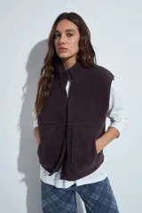 Chaleco de corderito color marrón oscuro, con cierre frontal completo, cuello alto y bolsillos laterales.