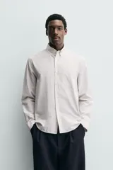 Camisa de corte regular fit confeccionada en tejido de algodón con estampado de cuadros pequeños. Presenta cuello abotonado, manga larga con puños abotonados, bolsillo de plastrón en el pecho y cierre frontal con botones.