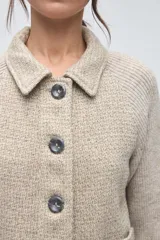 Campera corta con cuerpo de lana tejida en textura tweed y mangas de punto liso en color marrón. Presenta cuello camisero, cierre frontal con botones y bolsillos frontales tipo plaque.